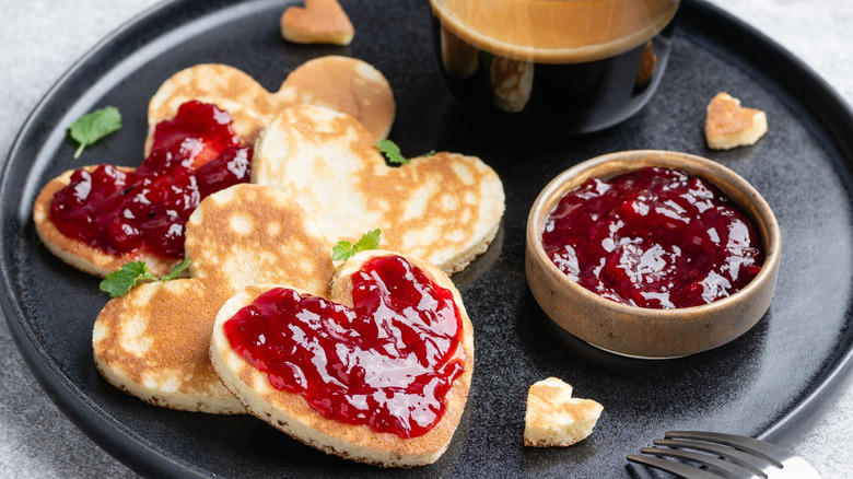 Little heart shaped pancakes topped with jam next to ramekin of jam