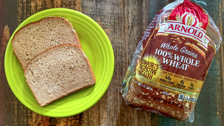 Two slices of Arnold Whole Grains 100% Whole Wheat bread next to a loaf of the same bread