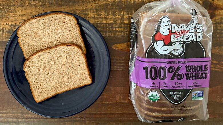 Two slices of Dave's Killer Bread 100% Whole Wheat bread next to a loaf of the same bread