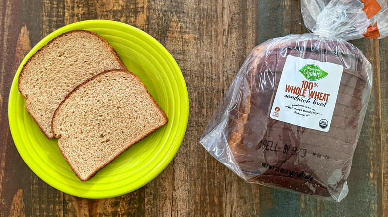 Two slices of Wegmans Organic 100% Whole Wheat Sandwich bread next to a loaf of the same bread
