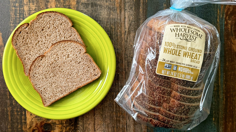 Two slices of Wholesome Harvest 100% Stone Ground Whole Wheat bread next to a loaf of the same bread