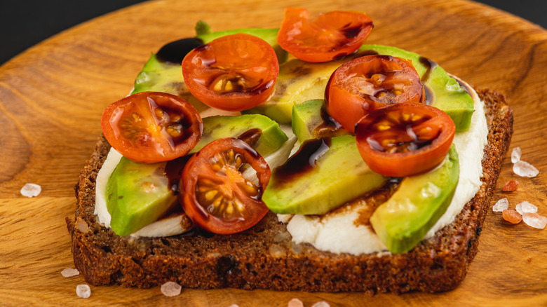 A slice of avocado toast topped with cherry tomato halves and balsamic vinegar drizzle