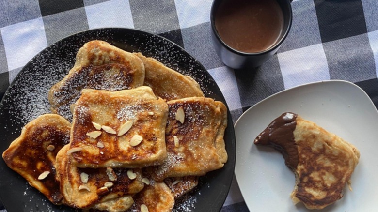 A plate full of almond pancakes with one on separate plate dipped in chocolate