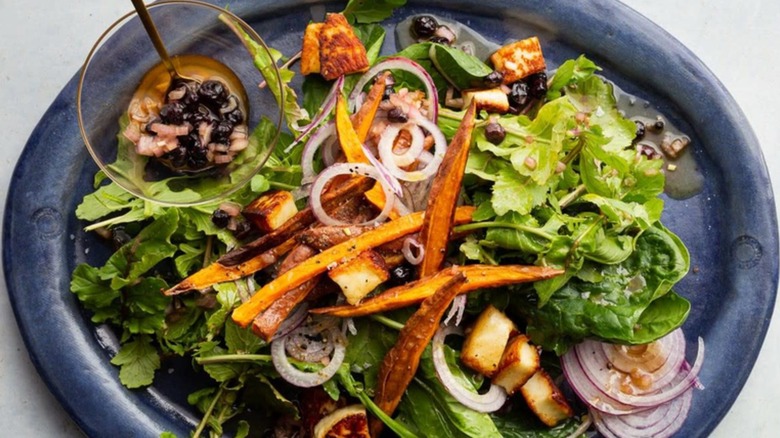 A platter of fresh salad greens dressed with sweet potatoes and haloumi