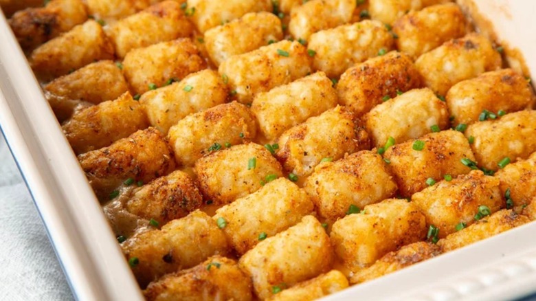 A closeup of creamy cheesy cowboy casserole topped with tater tots in ceramic tray