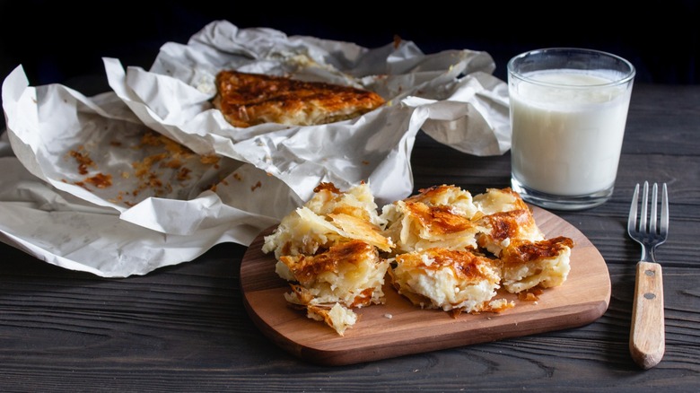 Burek or Borek savory pastry pie sliced on a board with a glass of drinkable yogurt