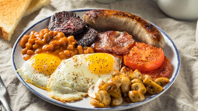 Homemade Full English breakfast with eggs, sausage, bacon, mushrooms, and baked beans