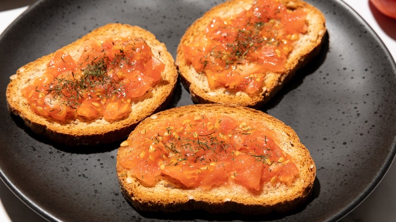 Three slices of toast topped with tomato on a black plate