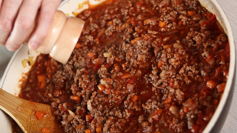 Hand grinding fresh pepper into meat sauce that is simmering in a pan