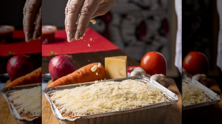 Hand adding freshly grated cheese to the top of lasagna before baking