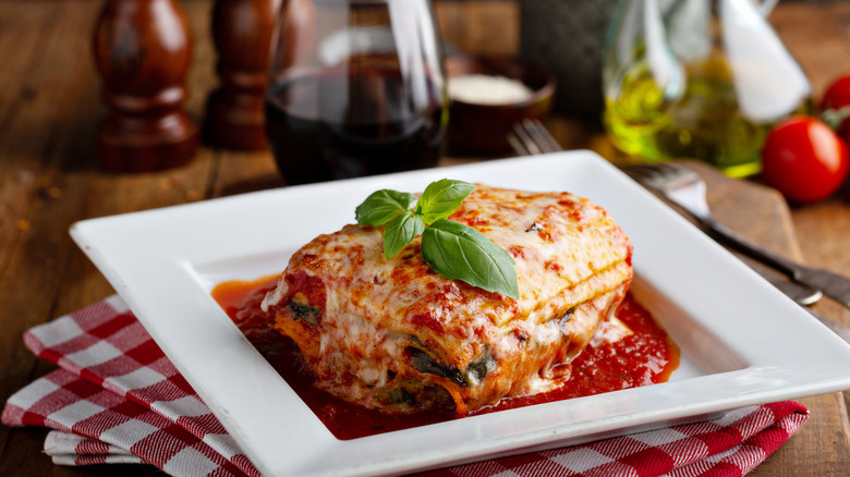 Slice of lasagna garnished with a sprig of basil on a square, white plate
