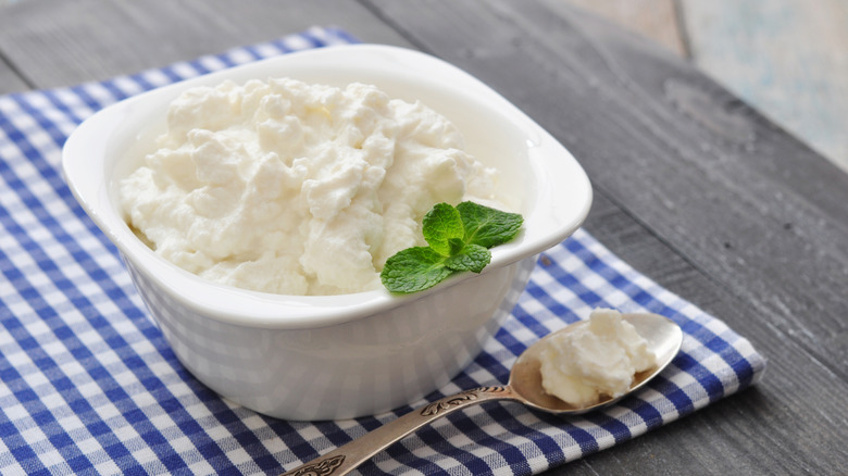 Ricotta in a white bowl garnished with fresh mint with a spoon on the side, all sitting atop a blue checkered napkin