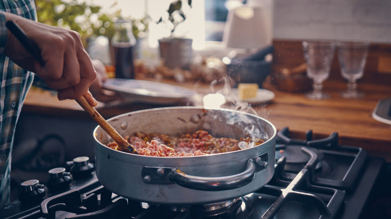 Hand stirring tomato sauce in a pan on stove top with a wooden spoon