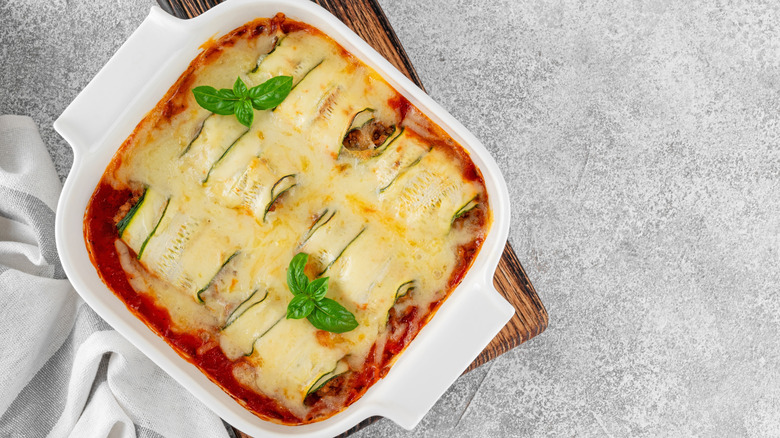 Roasted zucchini lasagna garnished with fresh sprigs of basil in a white casserole dish on a wooden cutting board