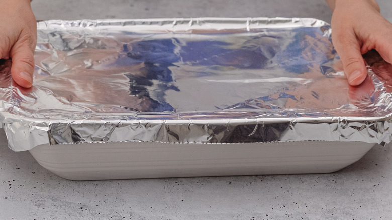 Hands pressing foil down onto casserole dish