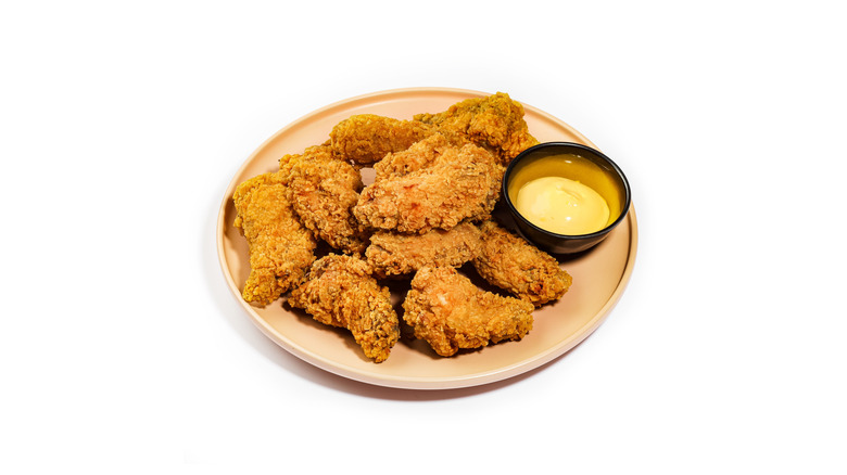 A plate of crispy fried wings with honey mustard on the side, isolated on a white background