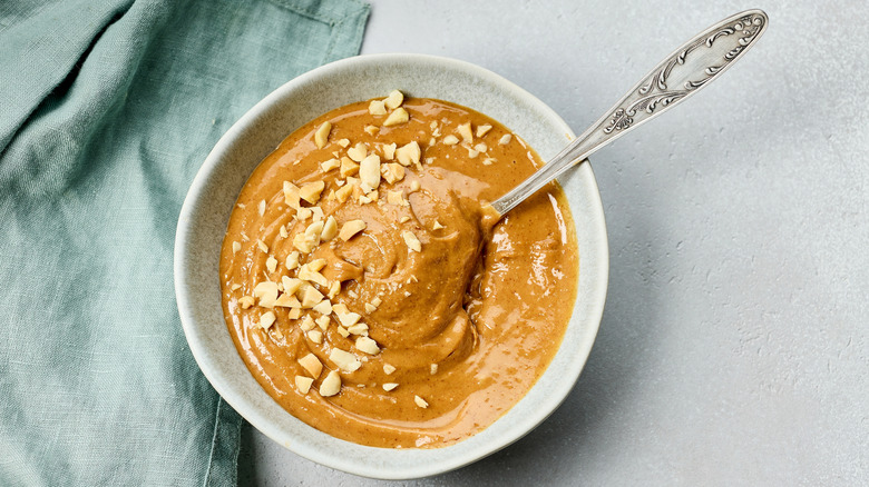Peanut sauce in a bowl with a spoon shot on a neutral backdrop with a linen dish towel