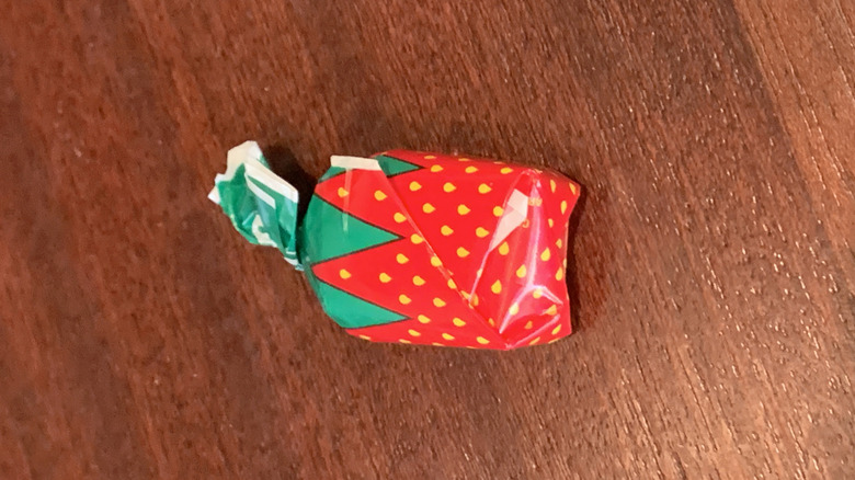 single wrapped strawberry bon bon on a wood-grained surface