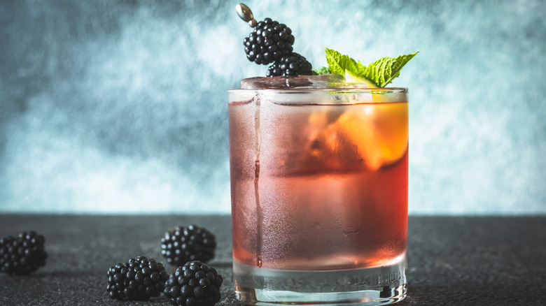 A rocks with an amber liquid, garnished with fresh blackberries and a sprig of mint.