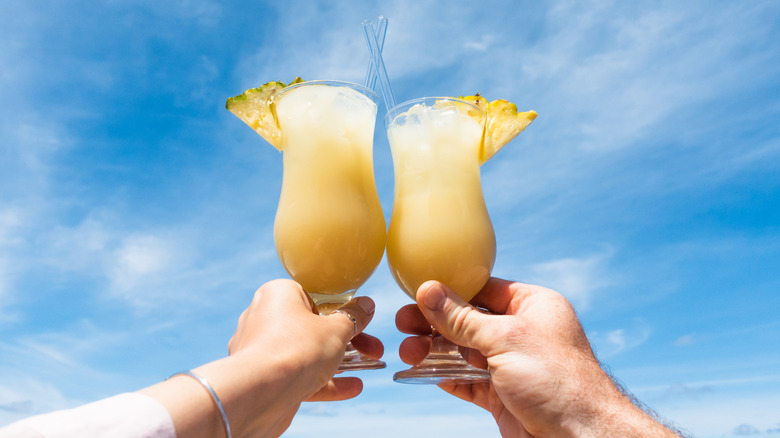 Two glasses filled with a pale yellow liquid are clinked together against a bright blue sky.