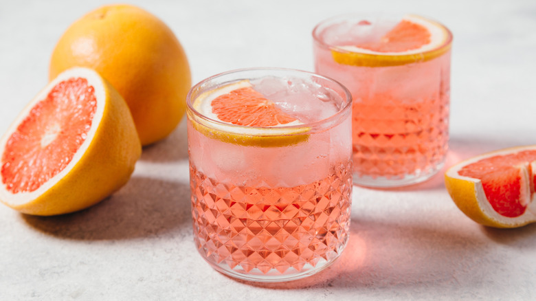 A light pink liquid over ice in a small glass next to sliced citrus.