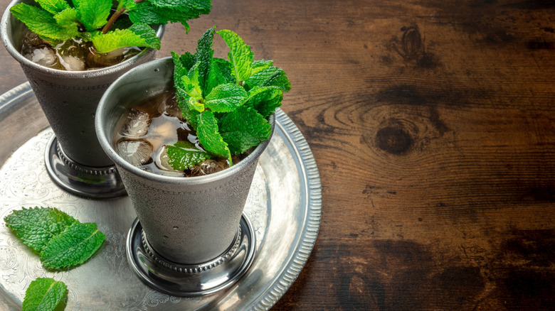 Two silver glasses on a tray with sprigs of fresh mint.