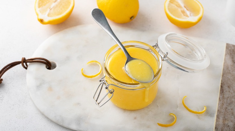 Lemon curd in a jar with a spoon on a marble tray
