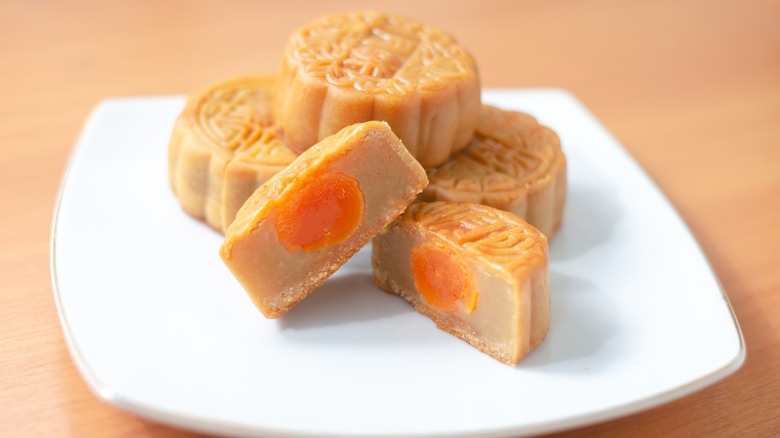 Mooncake on a white plate sliced open to reveal salted egg yolk inside