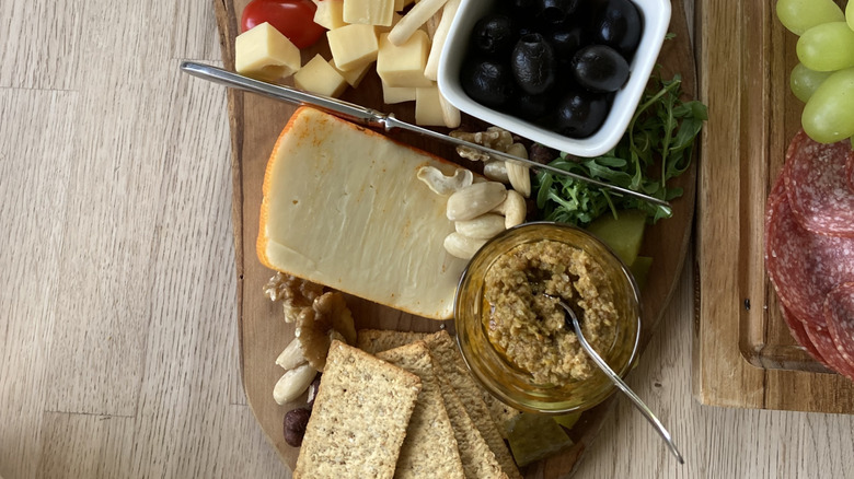 board with cheese, crackers, olives, and tapenade