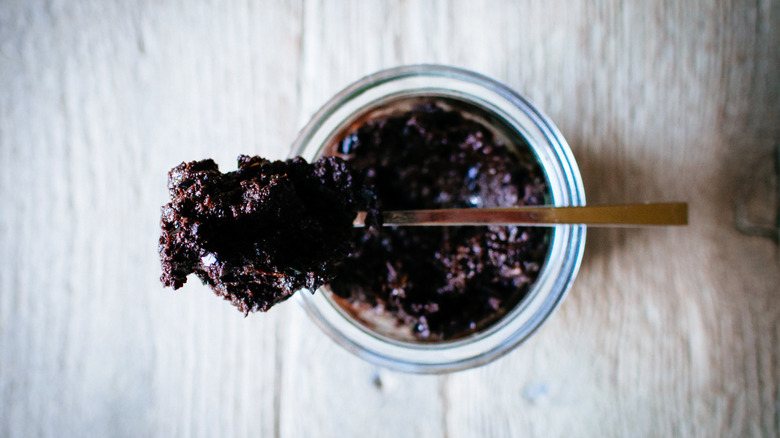 open jar of tapenade with a spoon balanced on the top