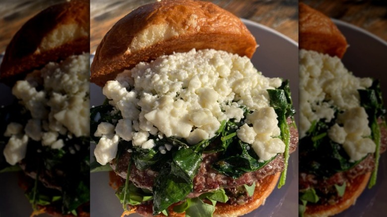 burger topped with tapenade, feta cheese, wilted spinach, and arugula