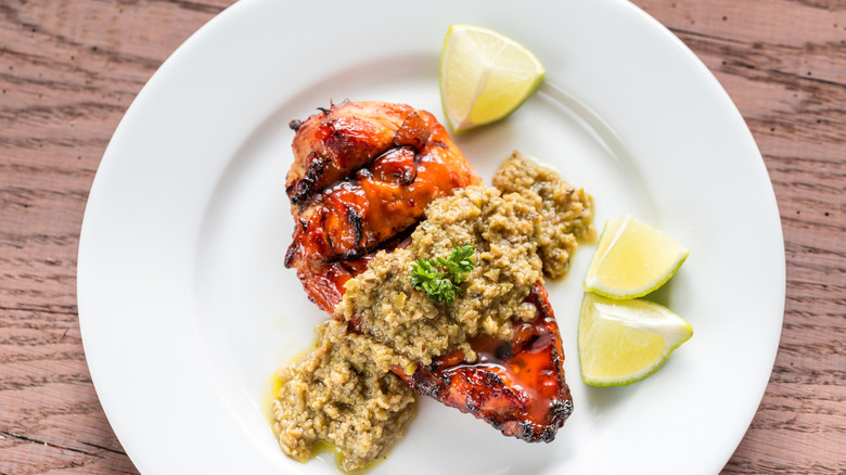 chicken covered with tapenade on a white plate with lemon wedges