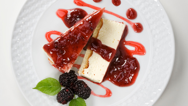Two slices of cheesecake on plate with berry drizzle and mulberry garnish
