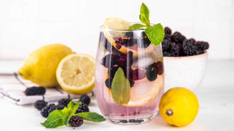 Glass filled with mulberry and lemon infused drink surrounded by fresh lemons and mulberries