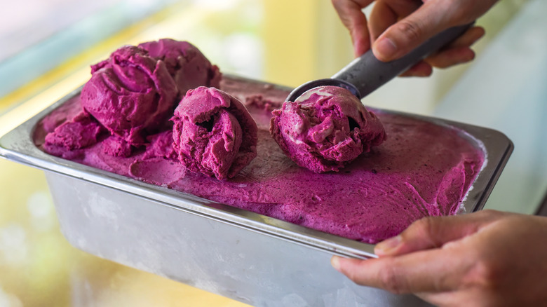 Balls of mulberry ice cream being scooped from metal container of ice cream