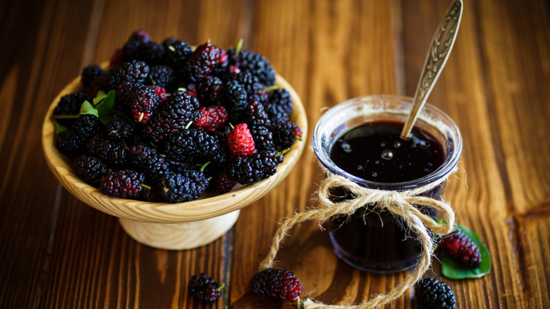 Bowl of fresh mulberries next to a glass jar of mulberry jam
