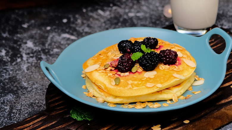 Stack of pancakes topped with mulberries, sliced nuts, and granola