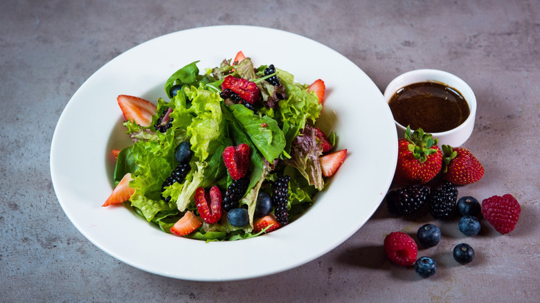 Bowl of salad topped with mix of strawberries, blackberries, and blueberries next to ramekin of fruit vinaigrette