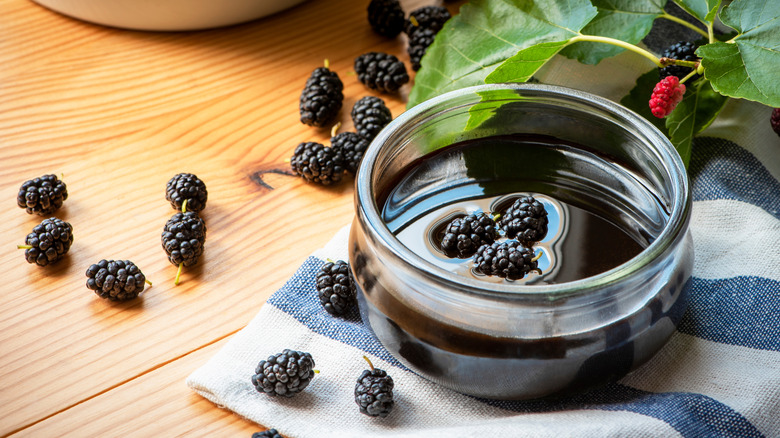 Glass bowl of mulberry syrup on cloth on wooden surface