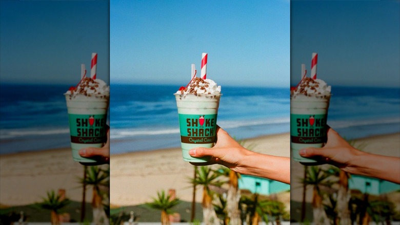 Hand holding Crystal Cove Shake Shack milkshake in front of ocean