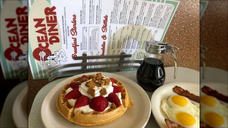 Ocean Diner menu behind waffle, eggs, bacon, and a jar of syrup