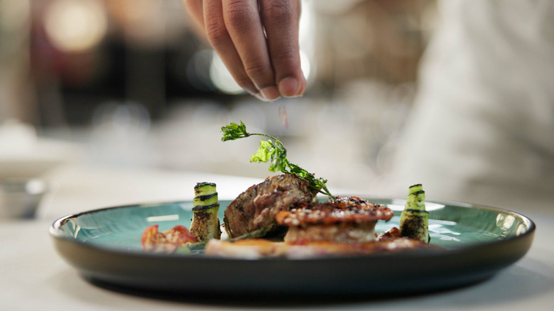 Hand sprinkling garnish onto plate