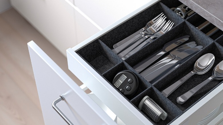 Uppdatera adjustable drawer organizer shown inside a kitchen drawer holding flatware and a thermometer