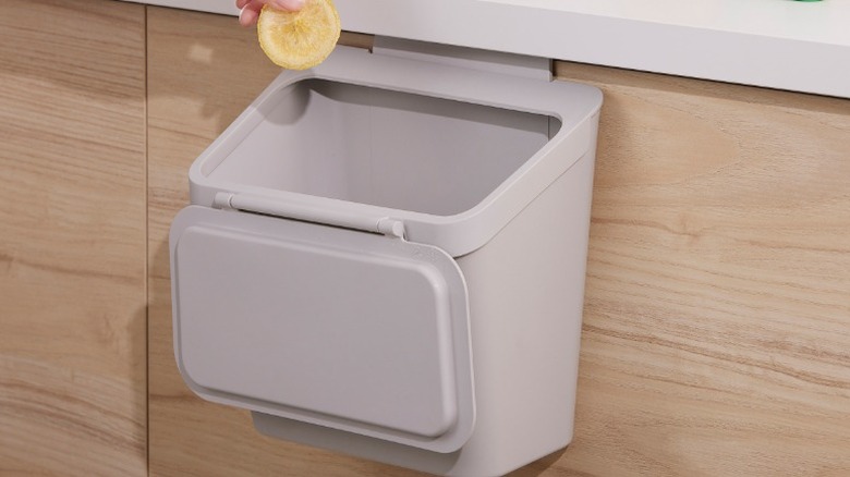 hand putting a lemon slice into a Skoläst mini trash can hanging from the door of a kitchen cabinet