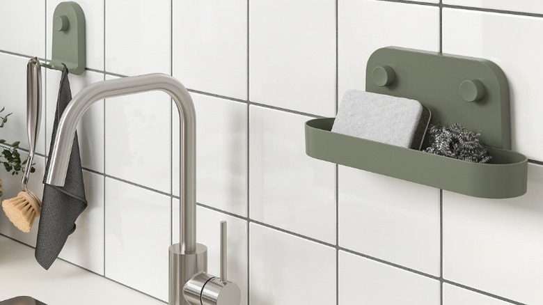 gray-green Öbonäs wall shelf with suction cup holding a sponge and a scrubber mounted on a wall next to a kitchen sink