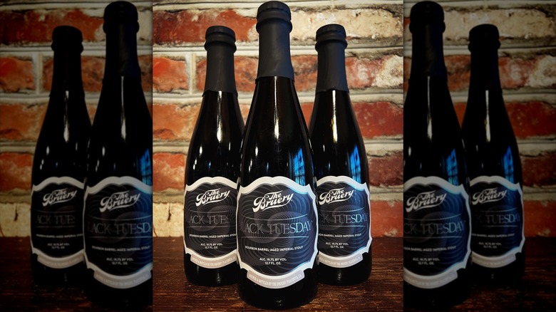 Three Black Tuesday beer bottles in front of brick wall