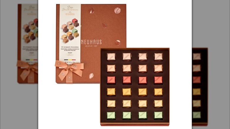 An open box of Neuhaus Les Savoureux chocolate pralines propped on a table surrounded by individual chocolates and a plate of shaved chocolate