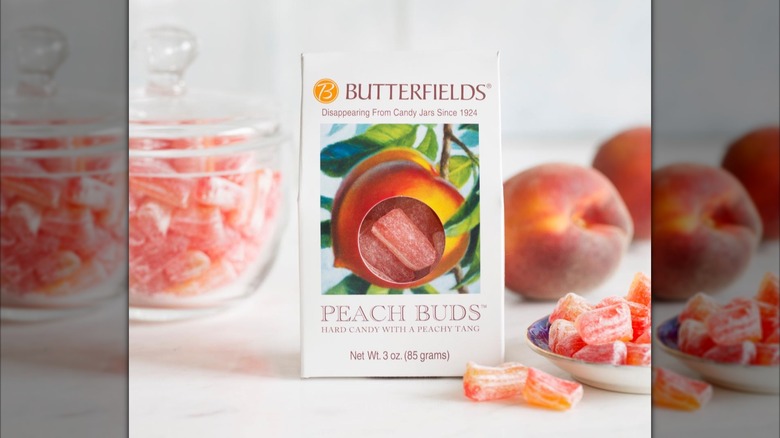 Butterfields Candy peach buds package on table with fresh peaches and some loose peach bud candies in a jar