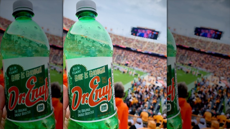 Dr. Enuf plastic soda bottle being held close to camera with a football stadium blurred in the background
