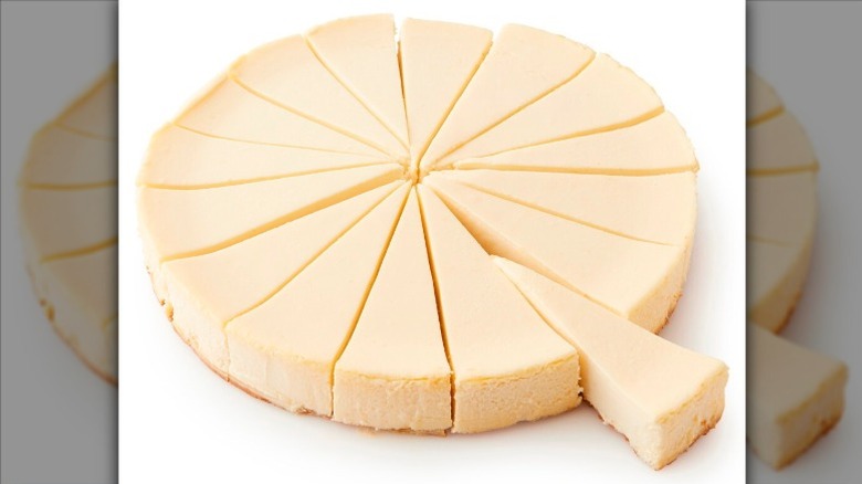 Private Selection Classic Creamstyle Cheesecake sliced into 16 pieces with one slice separated on a white background.